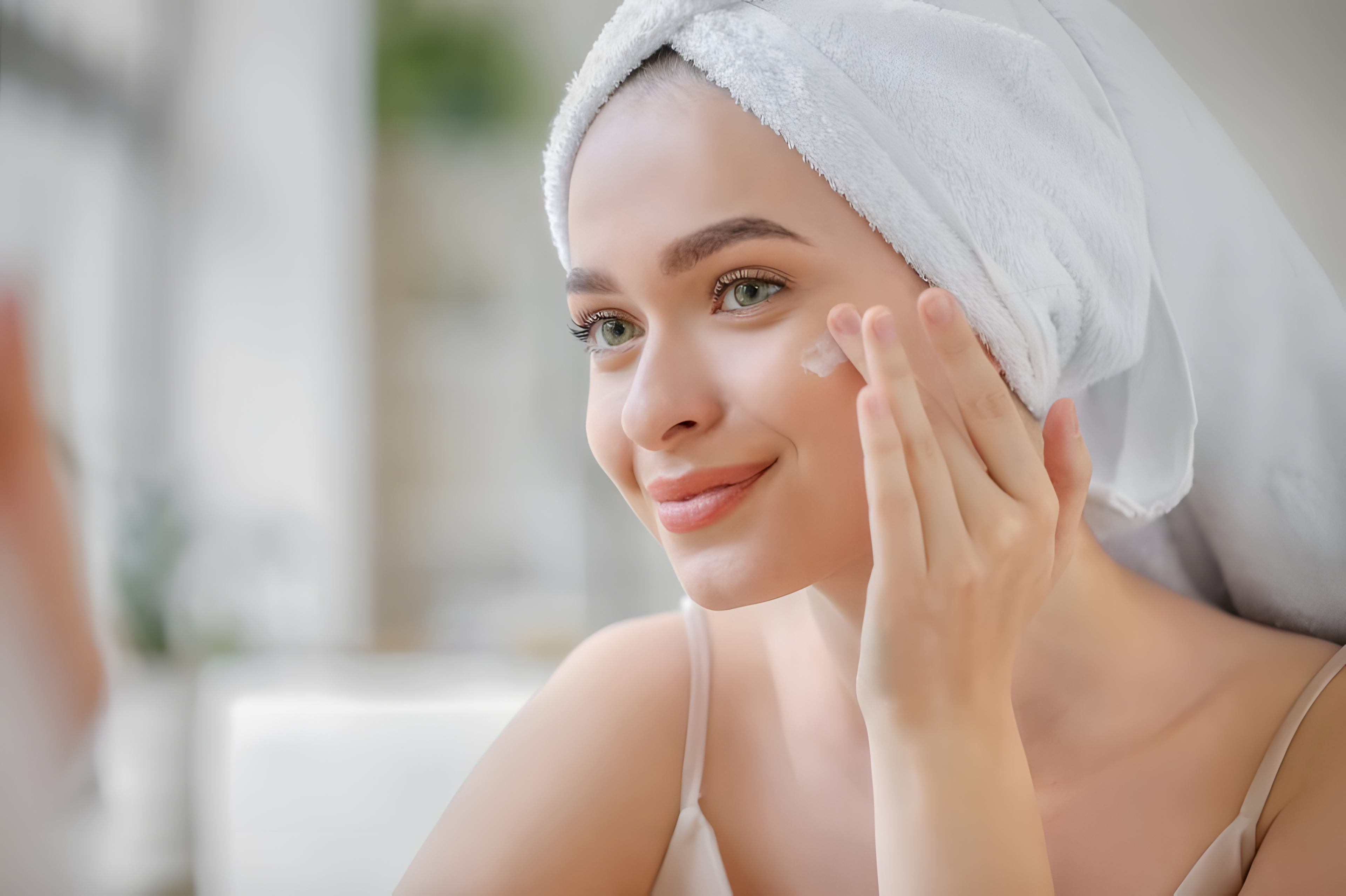 Woman applying cream to her face with a towel on her head, blurred background