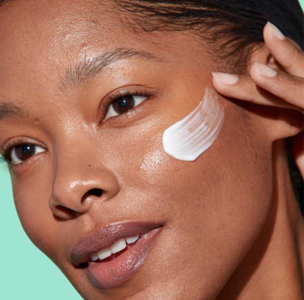 Woman applying white cream to her face against a teal background